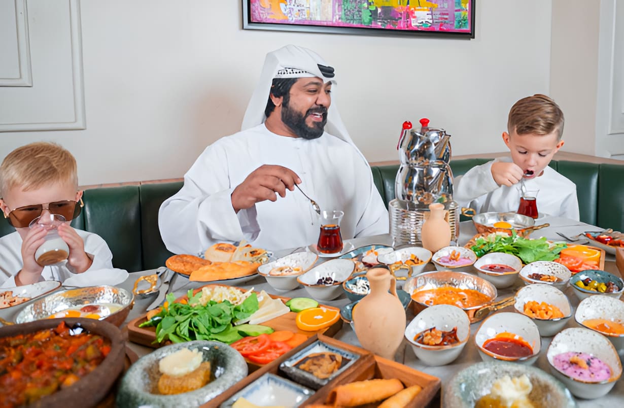 Emirati man and children enjoying a colorful Arabic mezze spread with traditional dishes like hummus, falafel, and fresh salads at a Middle Eastern restaurant.